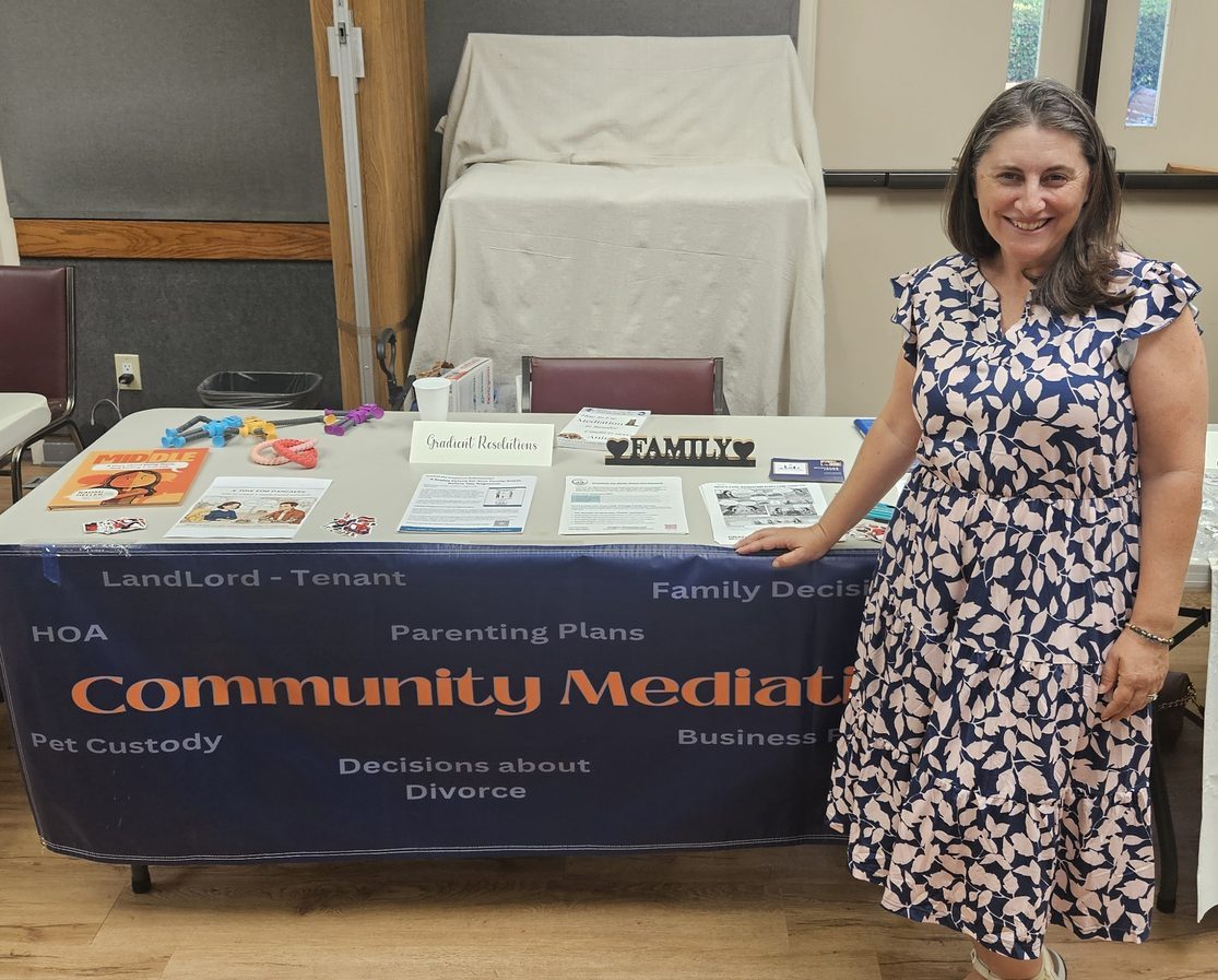 Laura Lorber smiling beside her Gradient Resolutions community mediation table at a local event